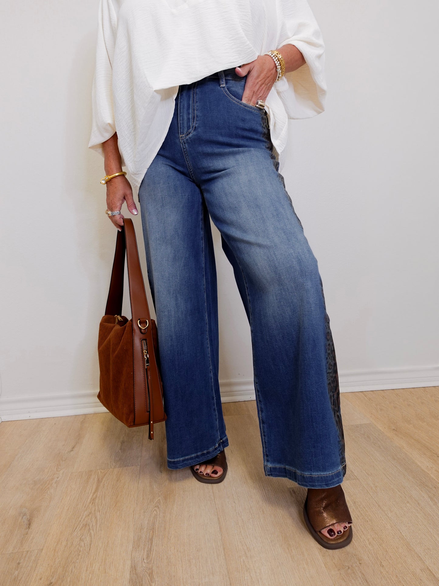 Person wearing blue jeans and a white top, holding a brown bag indoors.