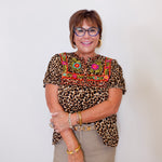 Woman wearing a leopard print top with colorful embroidery against a white background