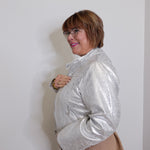 Woman wearing a silver jacket over a beige cardigan against a white background