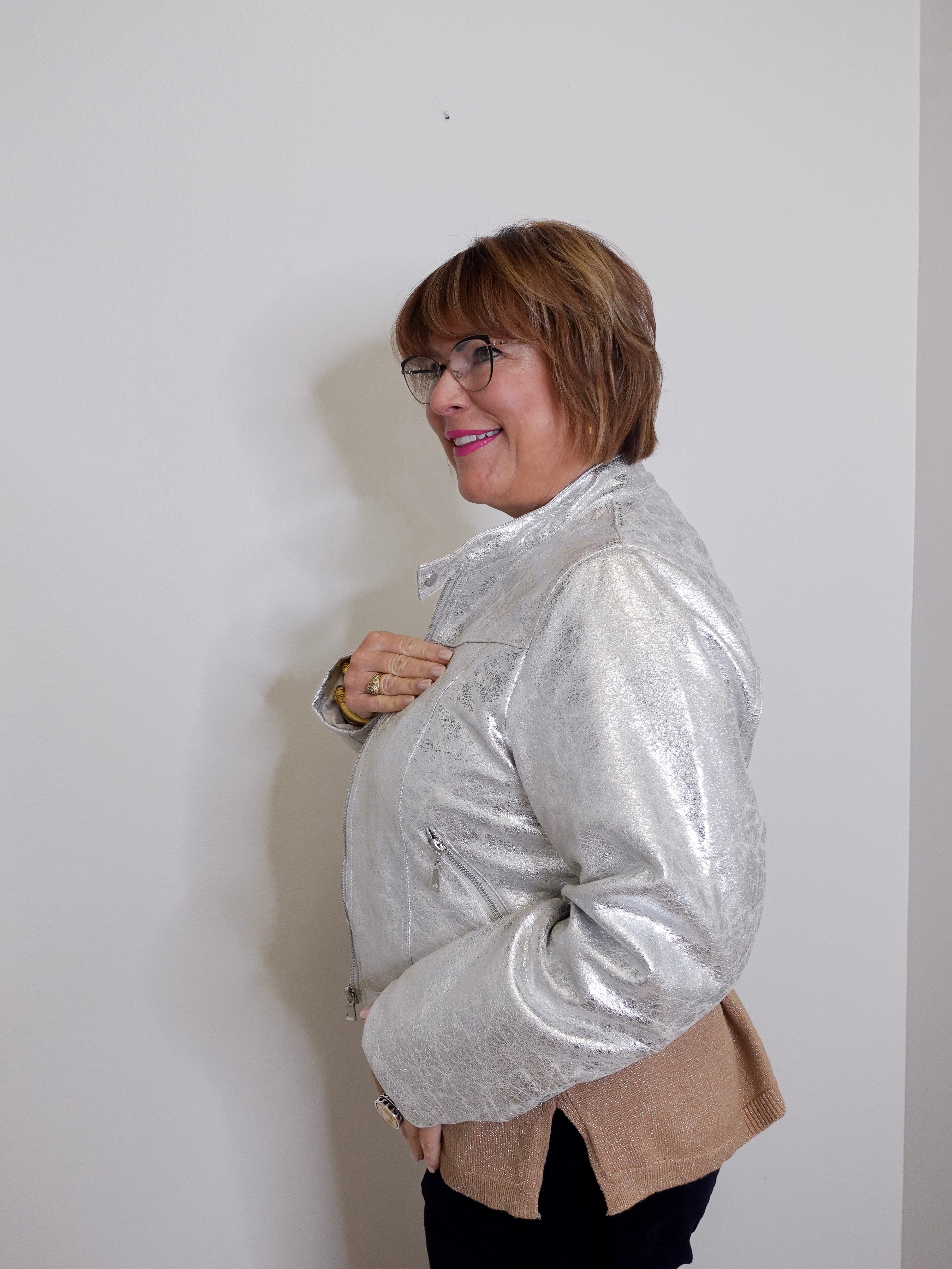 Woman wearing a silver jacket over a beige cardigan against a white background