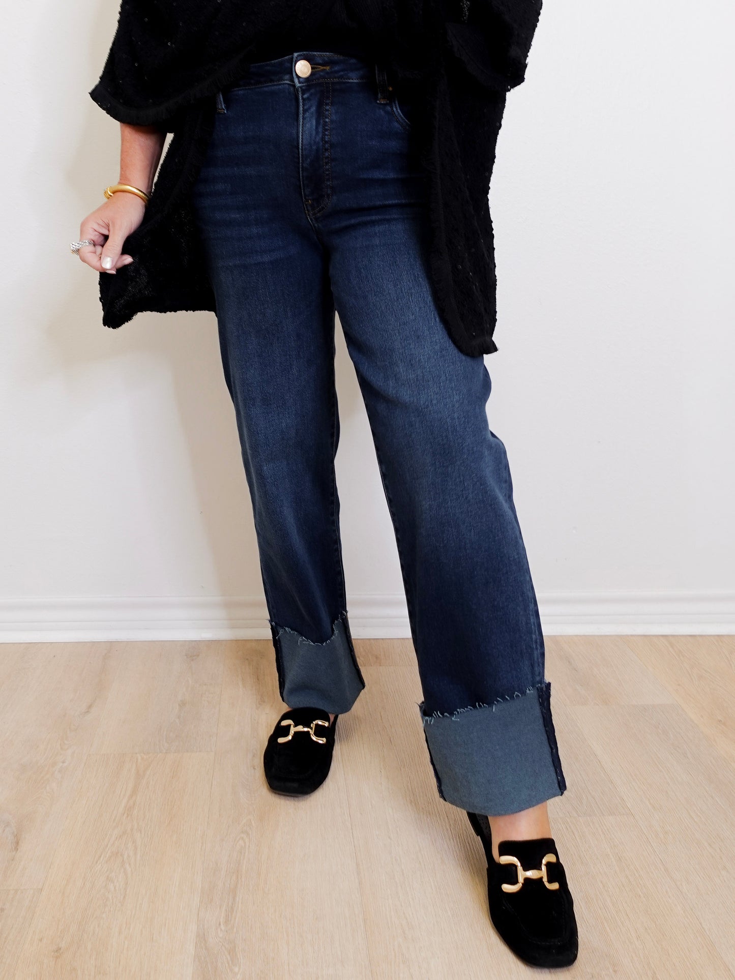 Person wearing dark blue jeans and black loafers on a light wooden floor.
