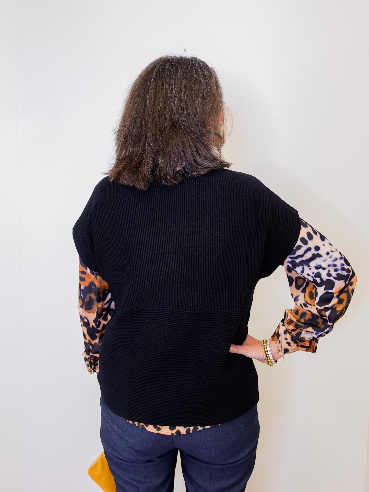 Person wearing a black sweater with leopard print sleeves underneath against a white background