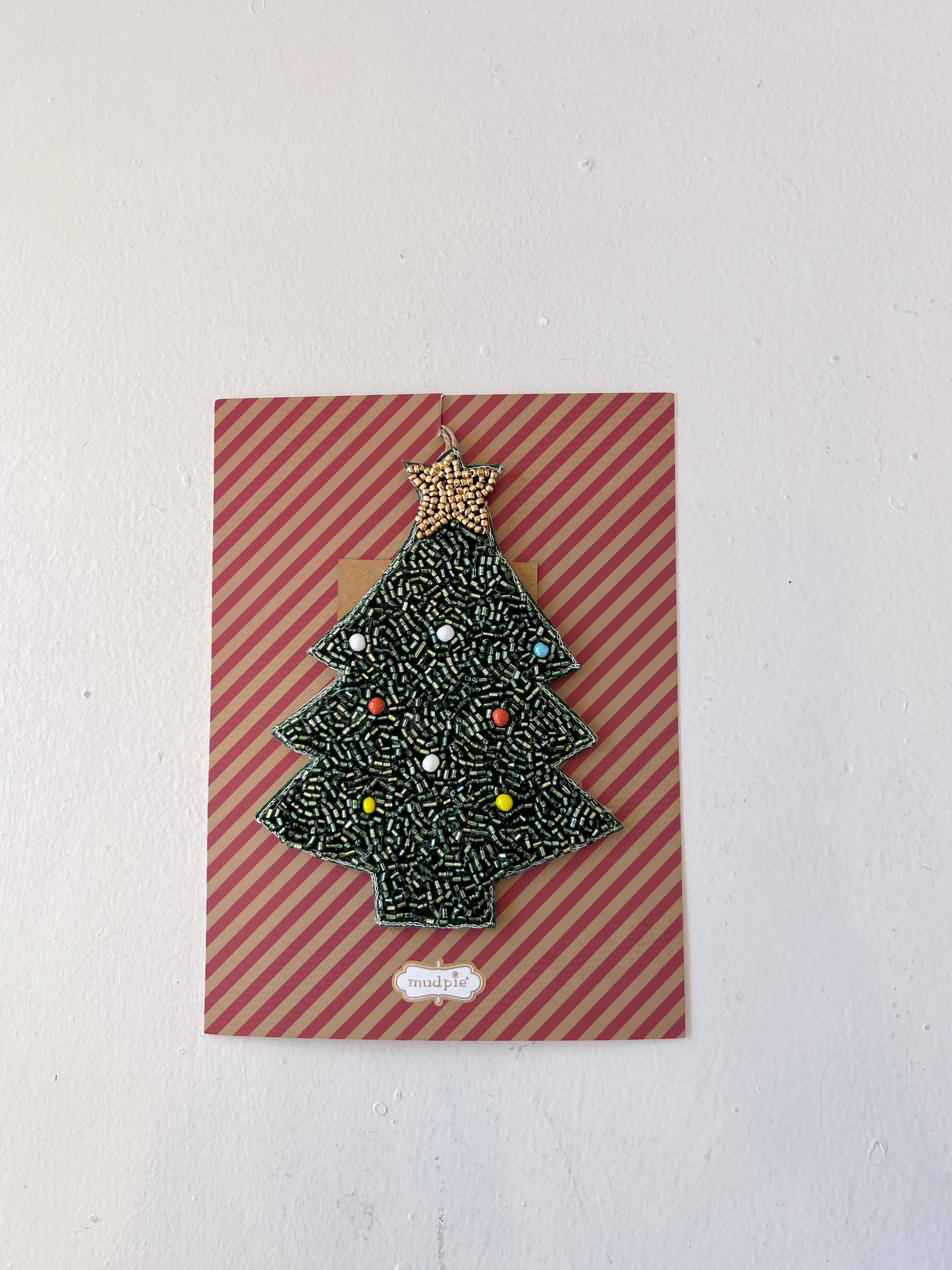 Christmas tree-shaped brooch on a striped card with a white background