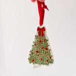 Hand holding a Christmas tree ornament with red berries and a red ribbon against a white background