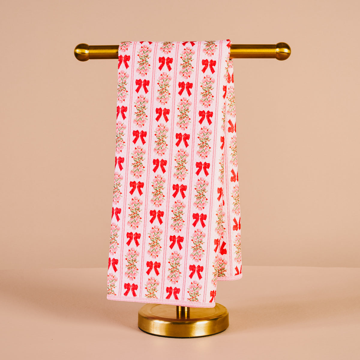 Towel with red bow pattern on a gold towel rack against a beige background