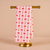Towel with red bow pattern on a gold towel rack against a beige background