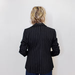 Person wearing a black pinstripe blazer against a white wall