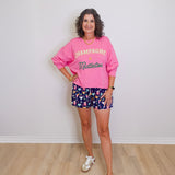 Woman wearing a pink sweatshirt with text and colorful shorts on a plain background