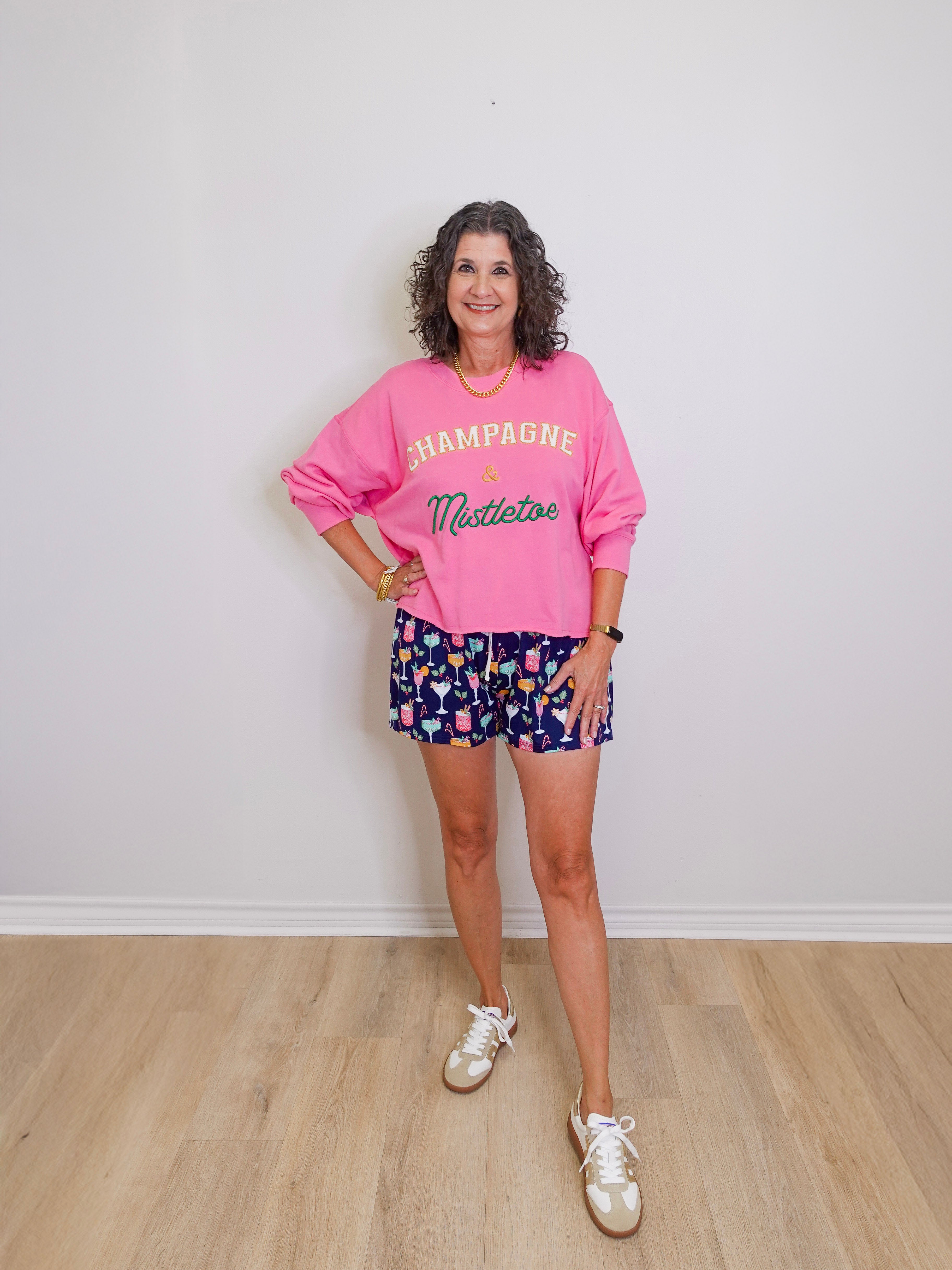 Woman wearing a pink sweatshirt with text and colorful shorts on a plain background