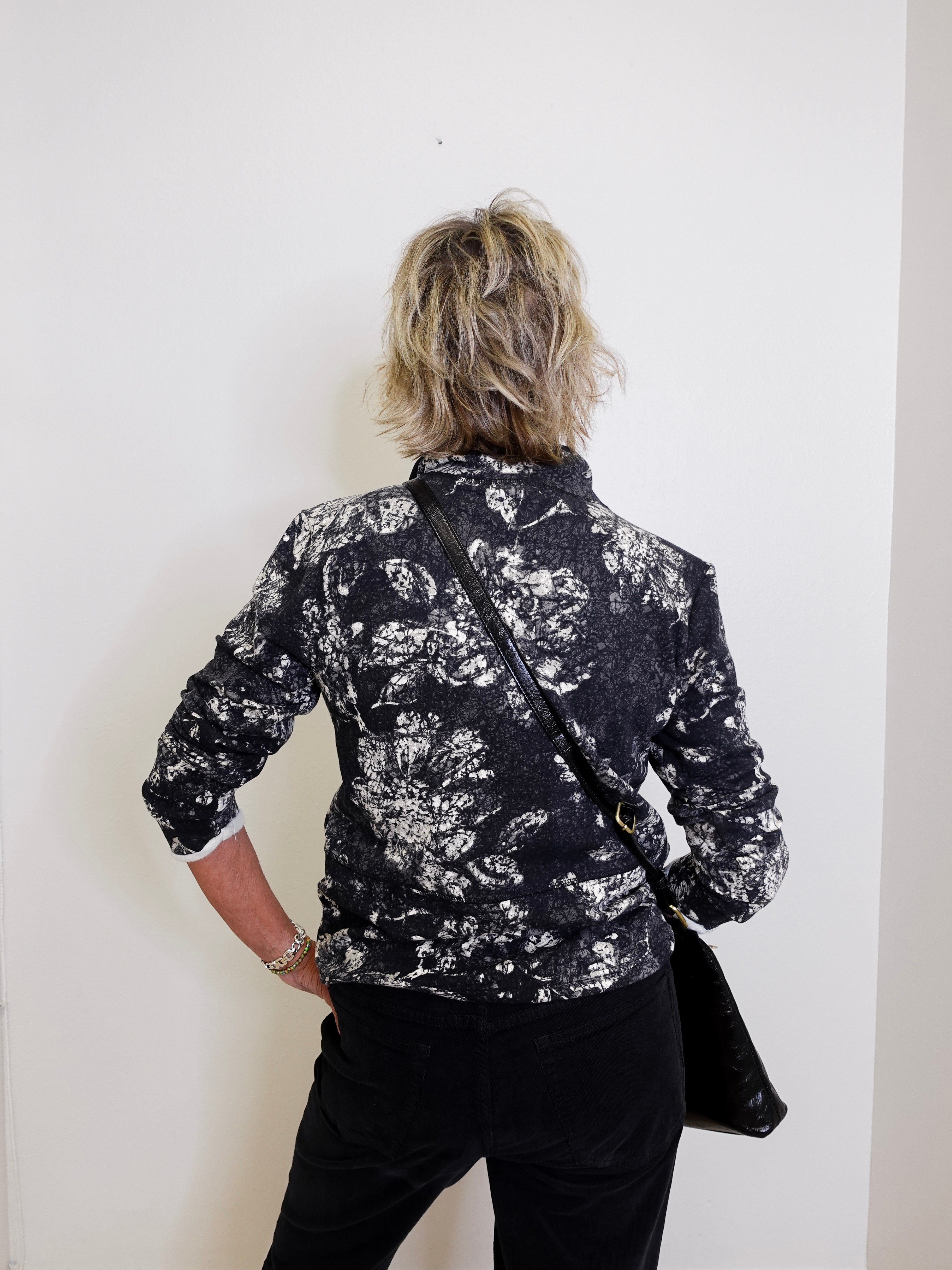 Person wearing a black and white patterned jacket against a white wall