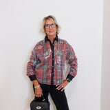 Person wearing a plaid jacket and holding a black handbag against a white background