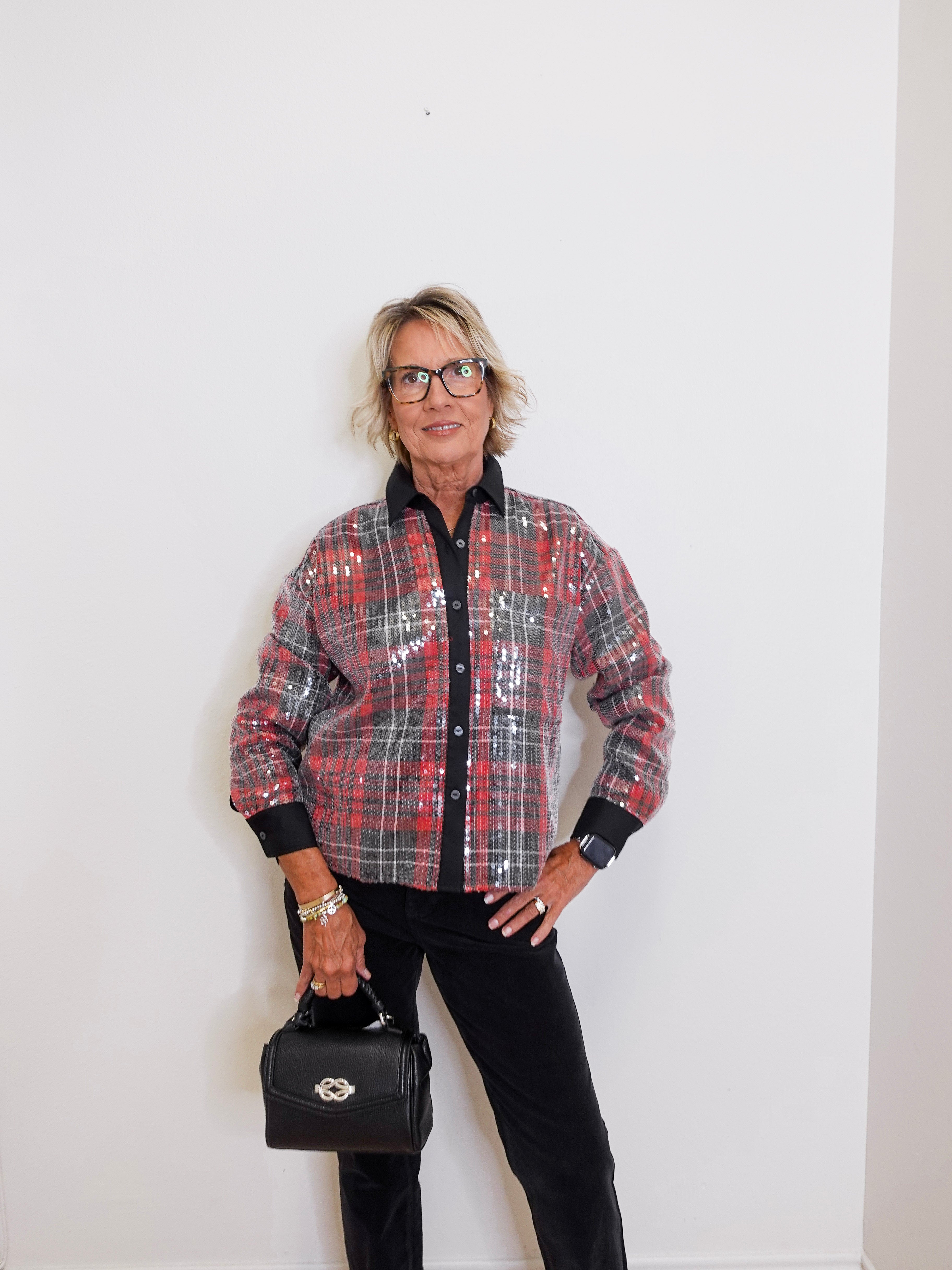 Person wearing a plaid jacket and holding a black handbag against a white background