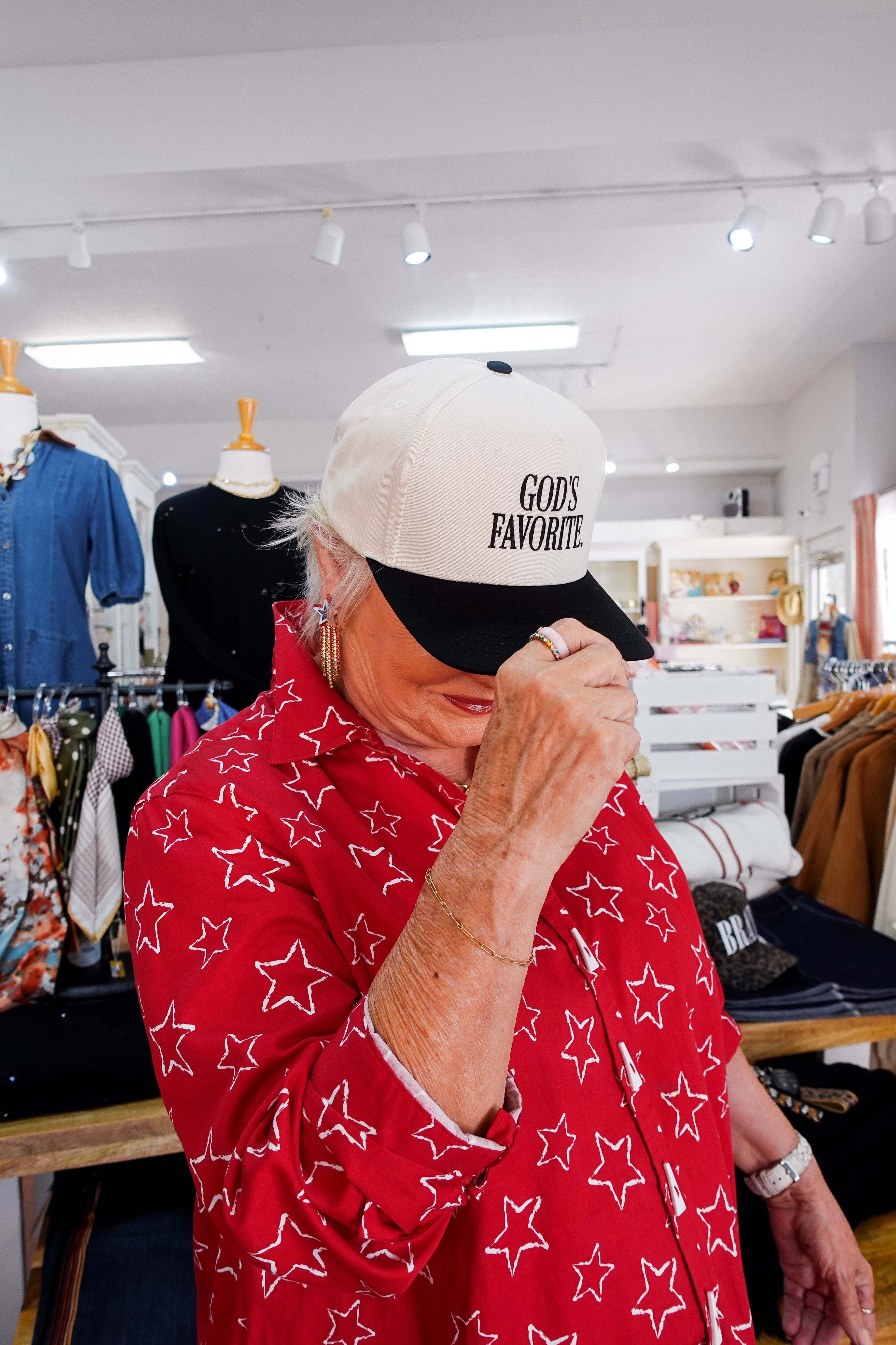 Person wearing a white cap with 'God's Favorite' text in a store setting