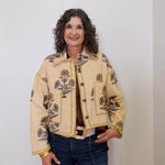 Woman wearing a beige jacket with floral patterns against a white background