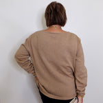 Person wearing a beige sweater against a white wall