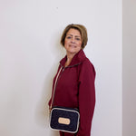 Woman in a burgundy outfit holding a navy blue handbag with a beige strap against a white background