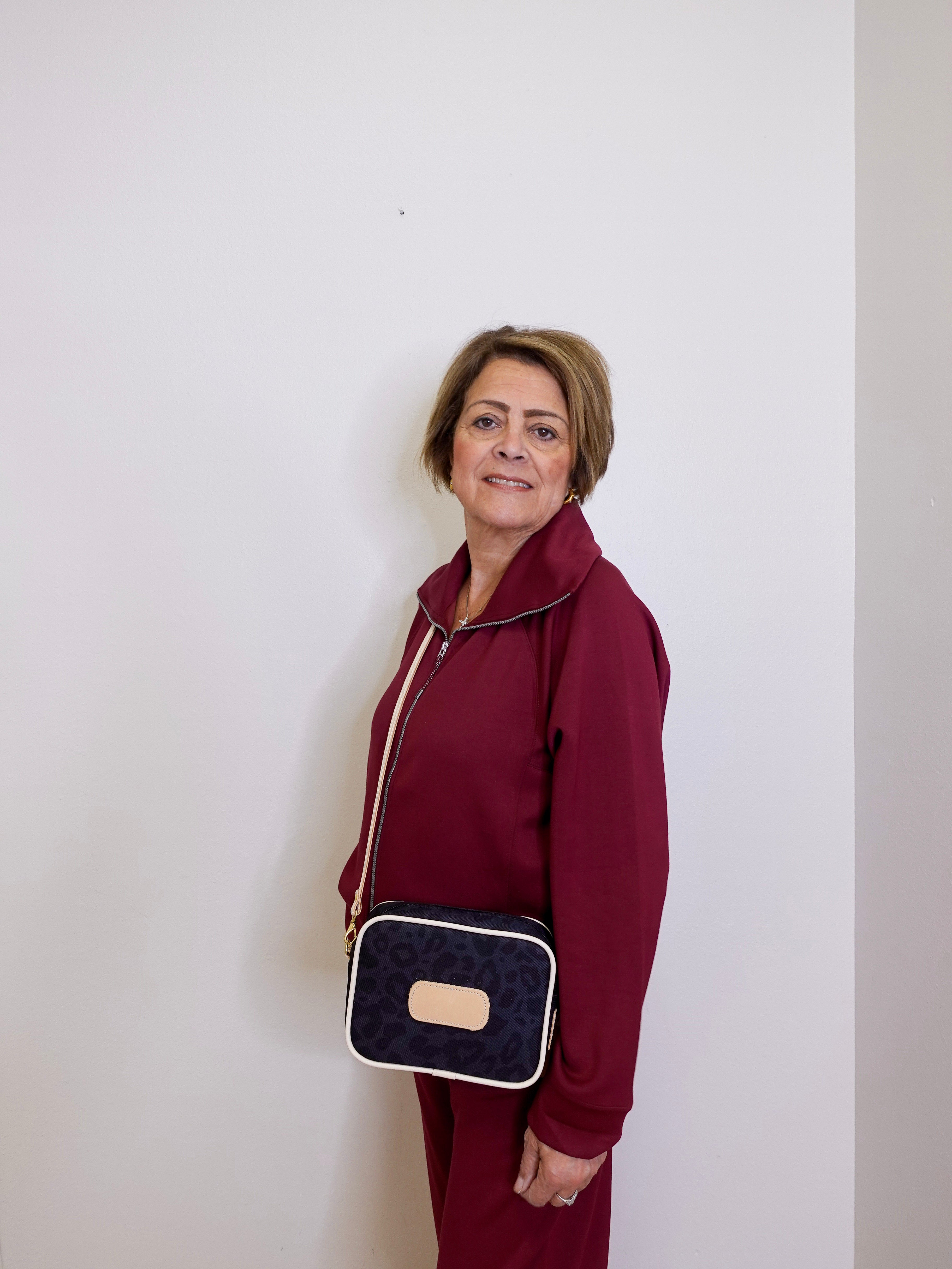 Woman in a burgundy outfit holding a navy blue handbag with a beige strap against a white background