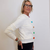 Woman wearing a white sweater with colorful buttons against a plain background