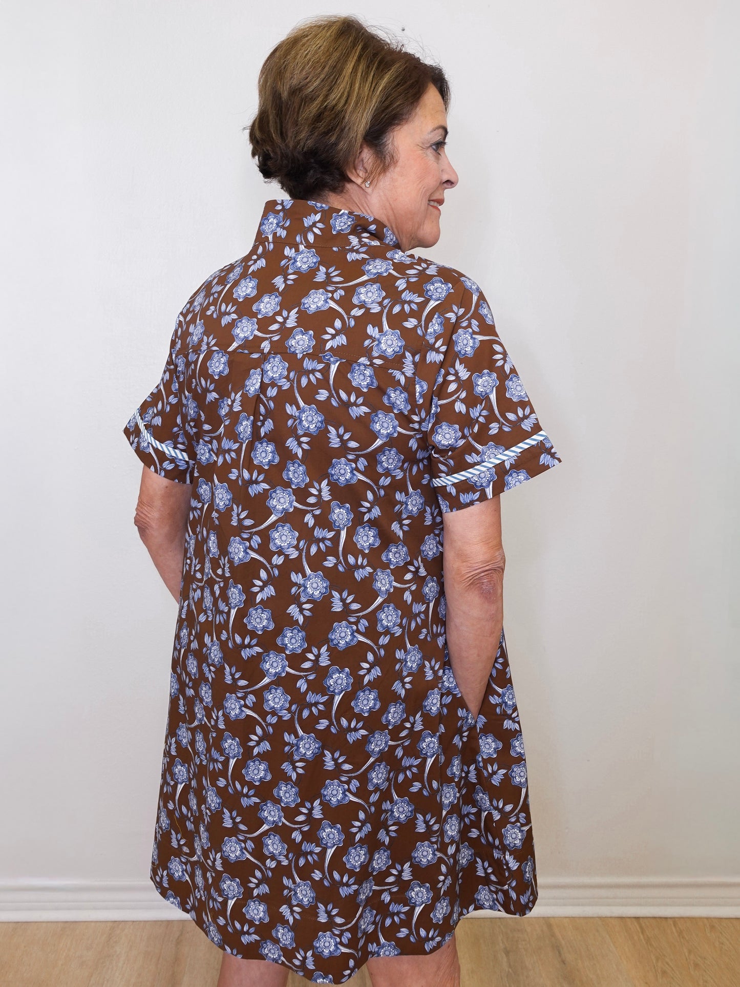 Woman wearing a brown floral dress against a white wall