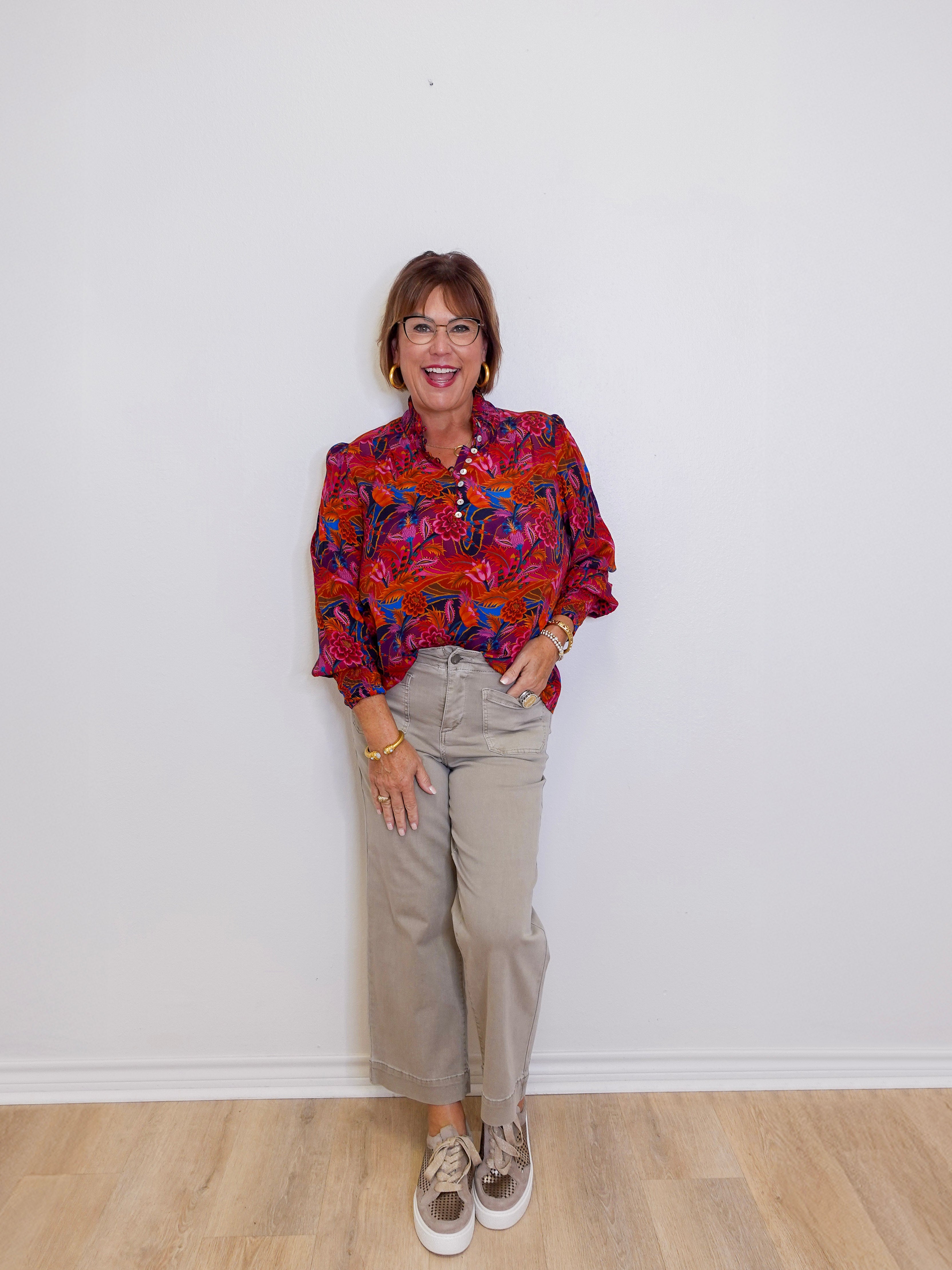 Person wearing a colorful patterned shirt and beige pants against a white wall.