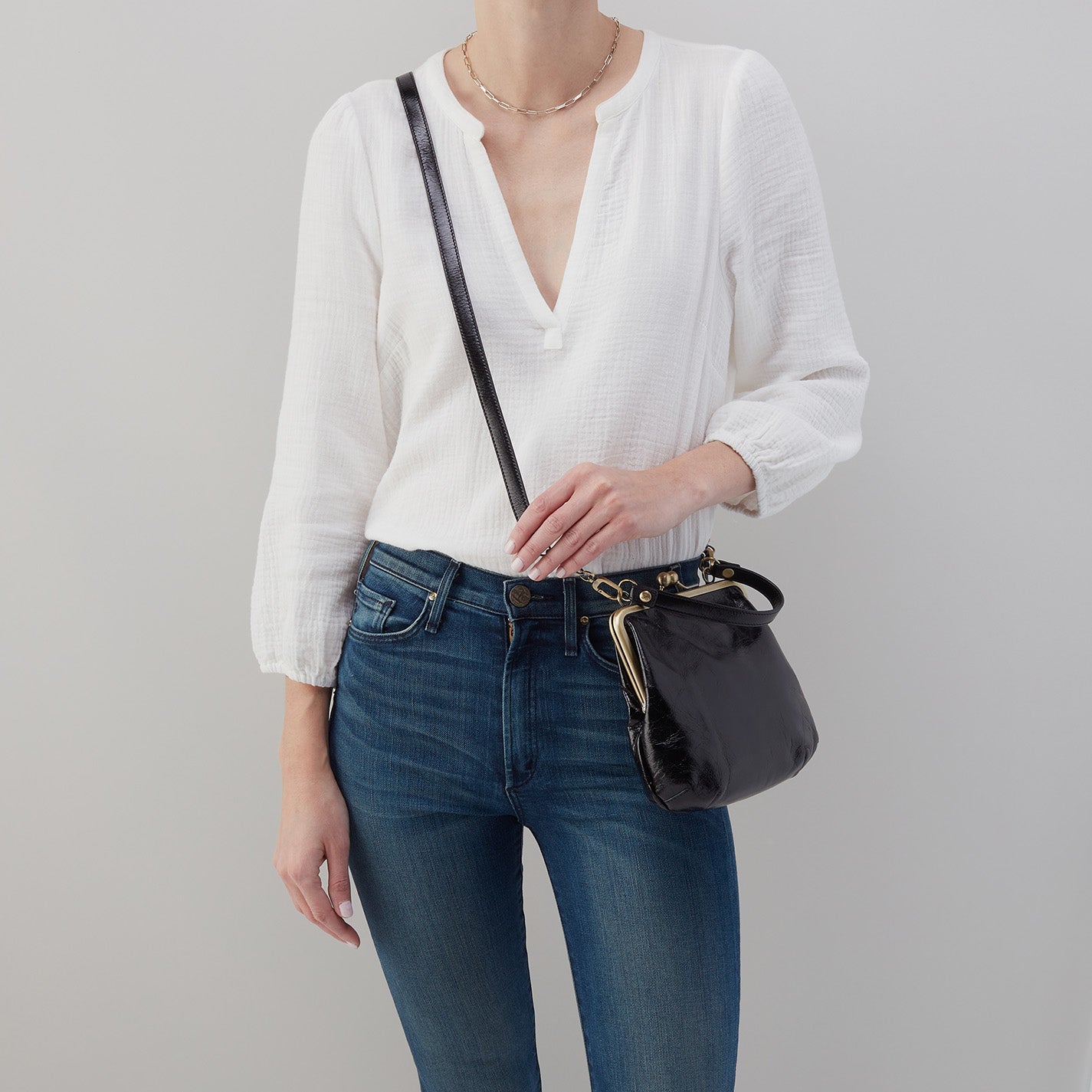 Person wearing a white blouse and blue jeans with a black handbag on a gray background