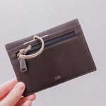 Brown leather wallet with a rope detail held by a hand on a light gray background