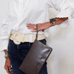 Person wearing a white shirt, blue jeans, and holding a brown leather bag on a plain background