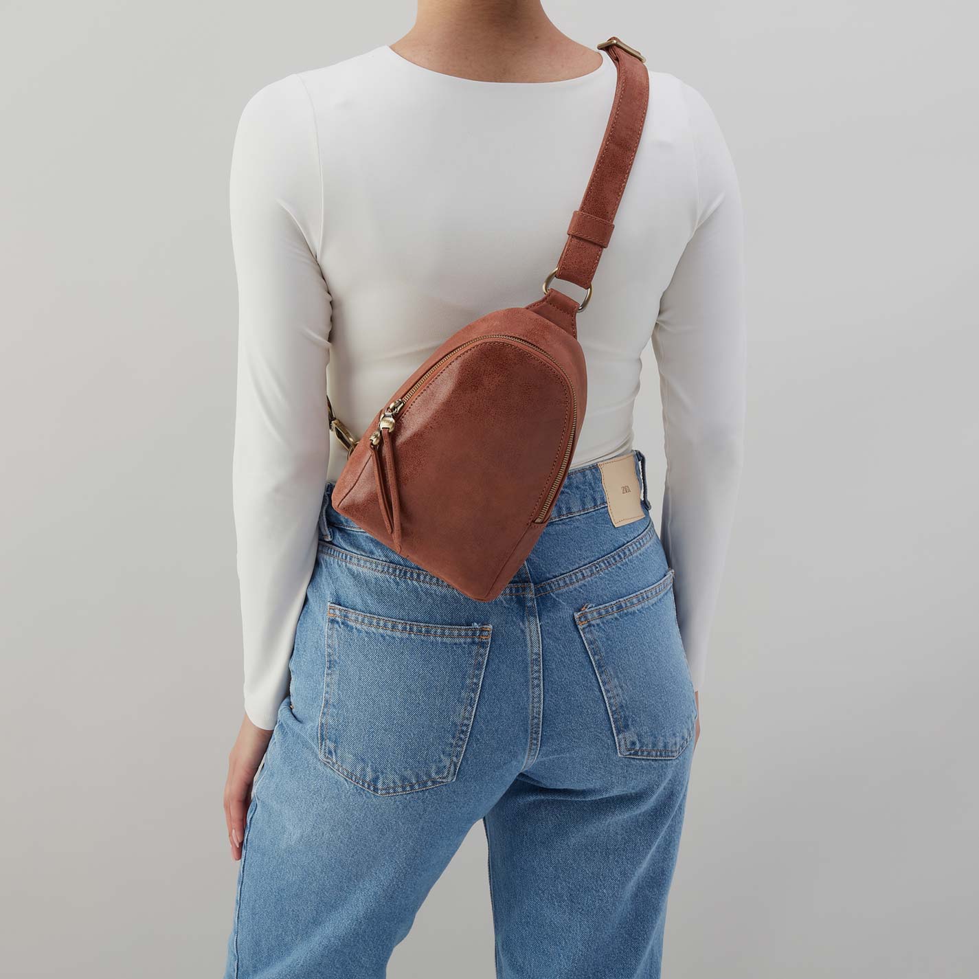 Person wearing a brown leather crossbody bag with a plain background