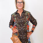 Woman wearing a leopard print shirt with floral sleeves, holding a brown handbag against a white background.