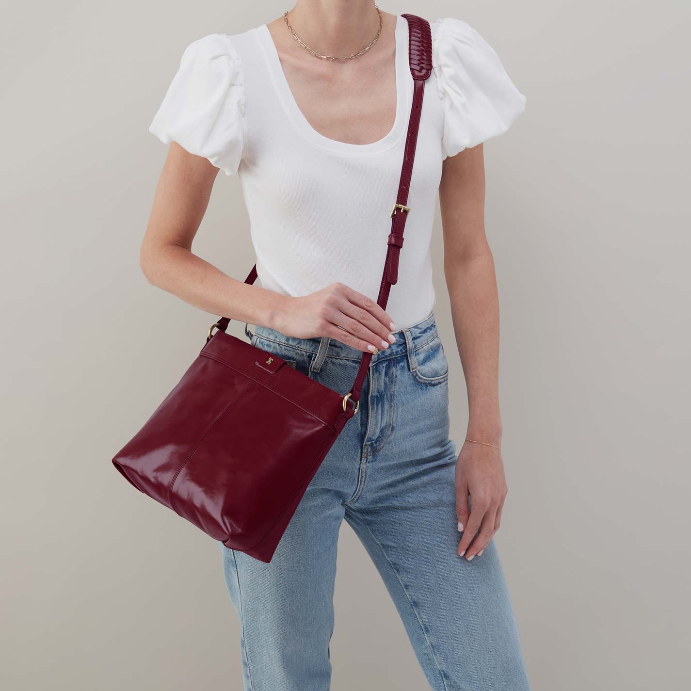 Person wearing a white top and blue jeans holding a maroon handbag against a neutral background