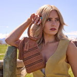 Woman holding a brown woven handbag outdoors with a clear blue sky.
