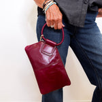 Person holding a maroon handbag against a plain background