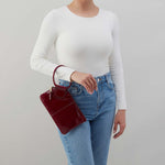 Person wearing a white long-sleeve top and blue jeans, holding a red handbag against a plain background