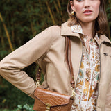 Woman wearing a beige coat and holding a brown handbag in a forest setting