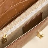 Close-up of a brown textured handbag with gold accents on a beige background
