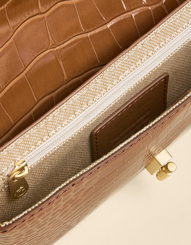Close-up of a brown textured handbag with gold accents on a beige background
