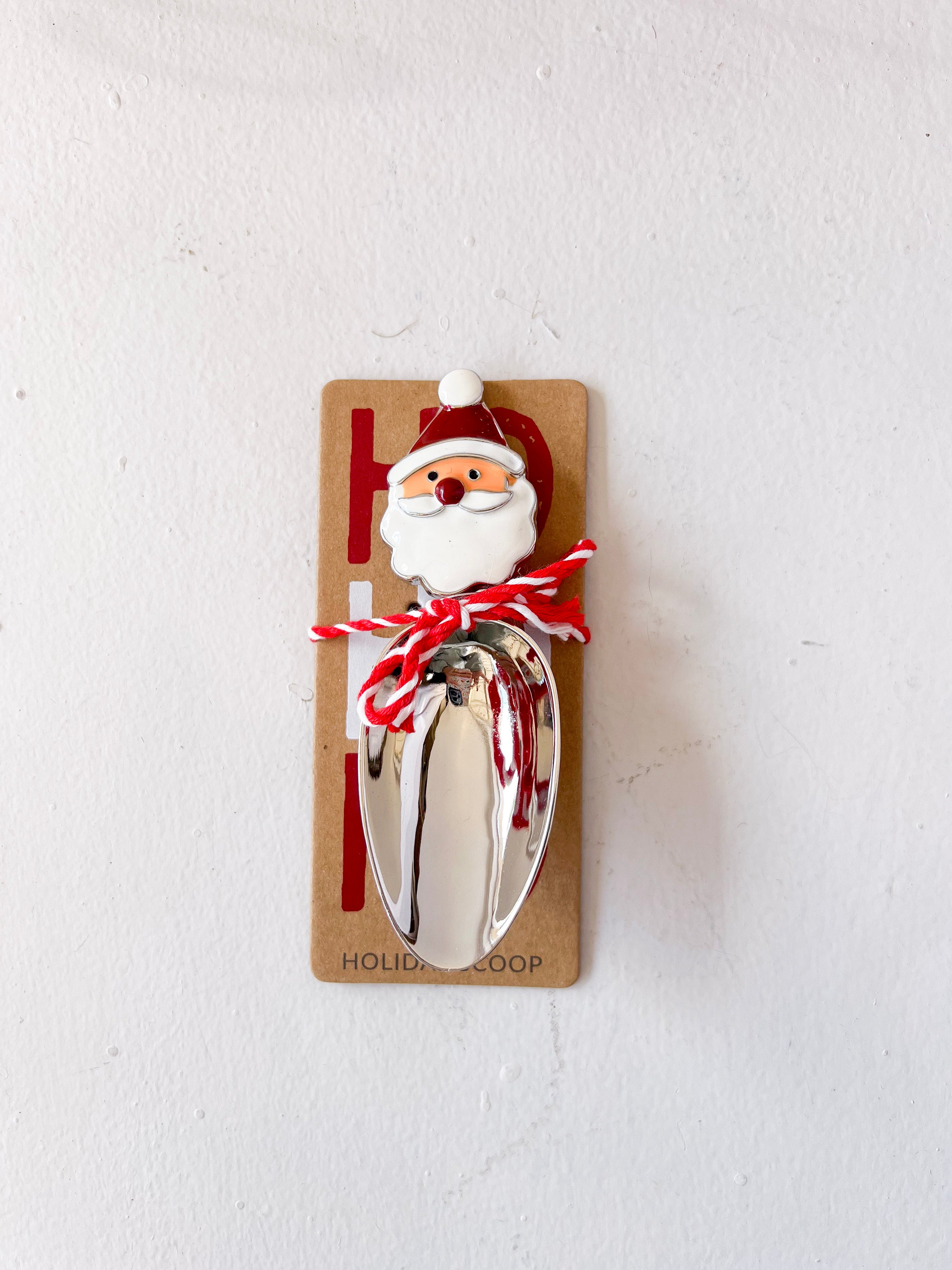 Metal scoop with Santa Claus design on a cardboard backing against a white background
