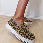 Leopard print sneakers with white soles worn by a person on a wooden floor.