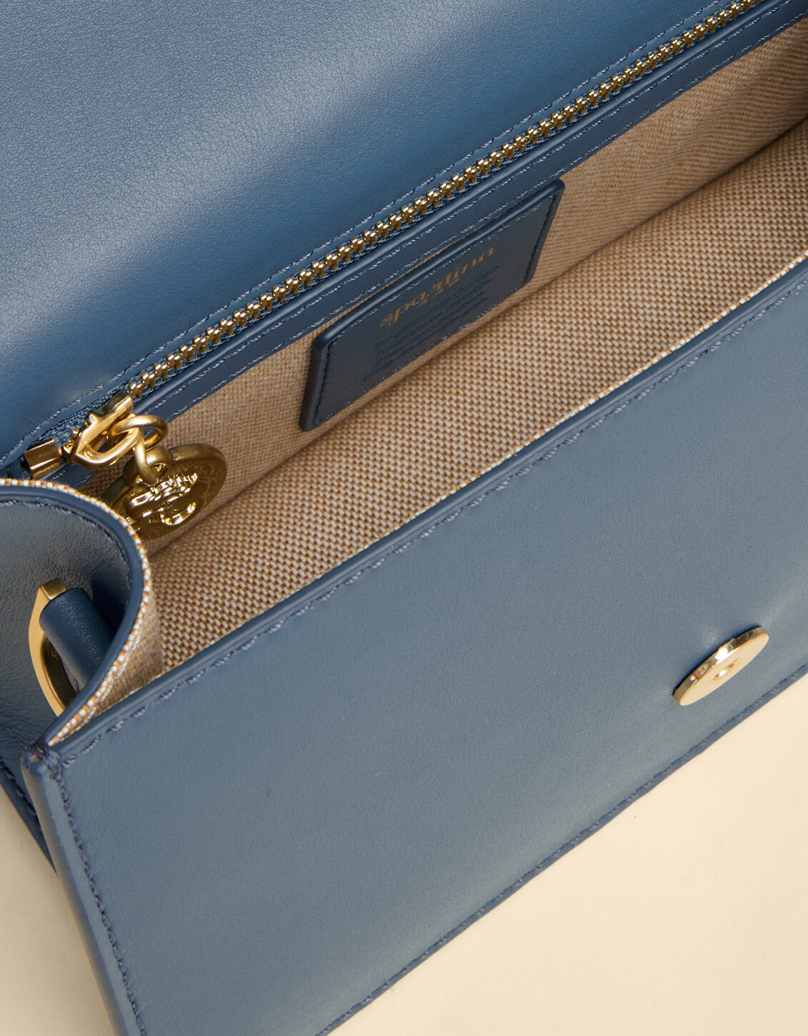 Close-up of a blue handbag with gold accents on a beige background