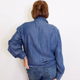 Person wearing a blue denim jacket and jeans against a white wall