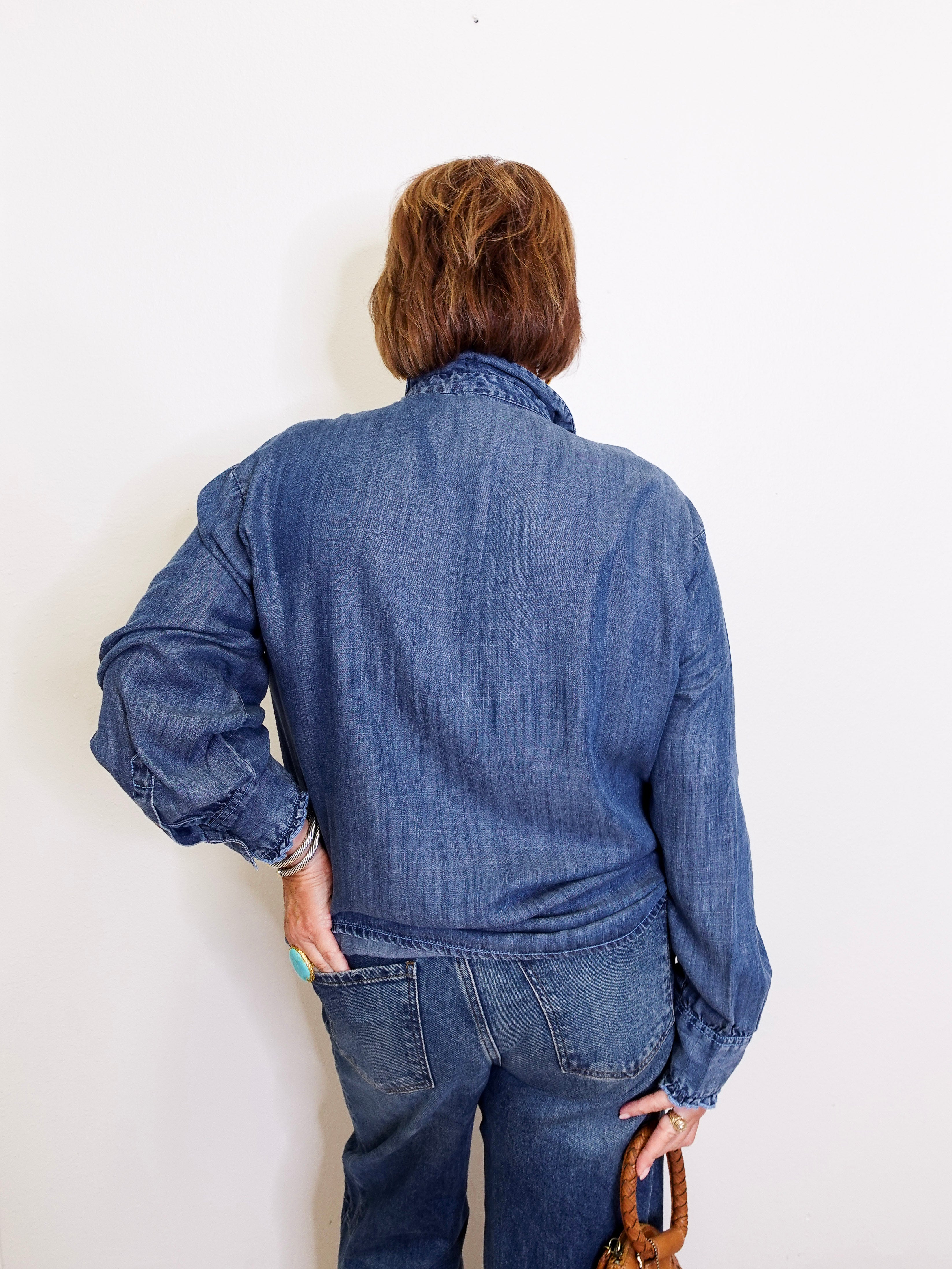 Person wearing a blue denim jacket and jeans against a white wall