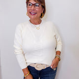 Woman wearing a white sweater and blue jeans, holding a brown clutch against a white background