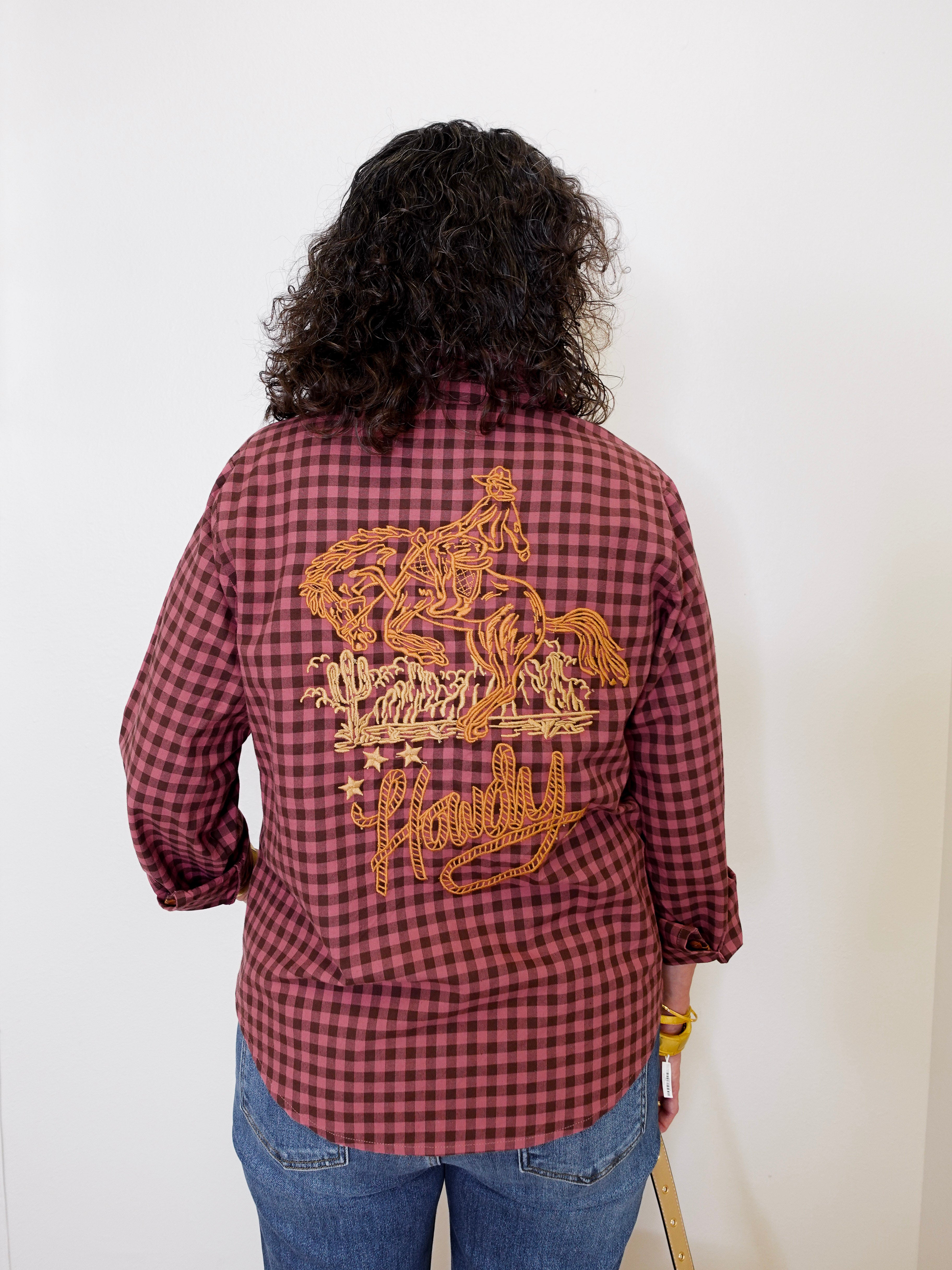 Person wearing a red plaid shirt with gold embroidery on the back, standing against a white background.