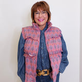 Woman wearing a floral patterned vest over a denim shirt against a plain background