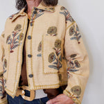 Woman wearing a beige embroidered jacket against a white background