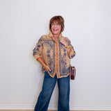 Woman wearing a patterned jacket and blue jeans against a white wall