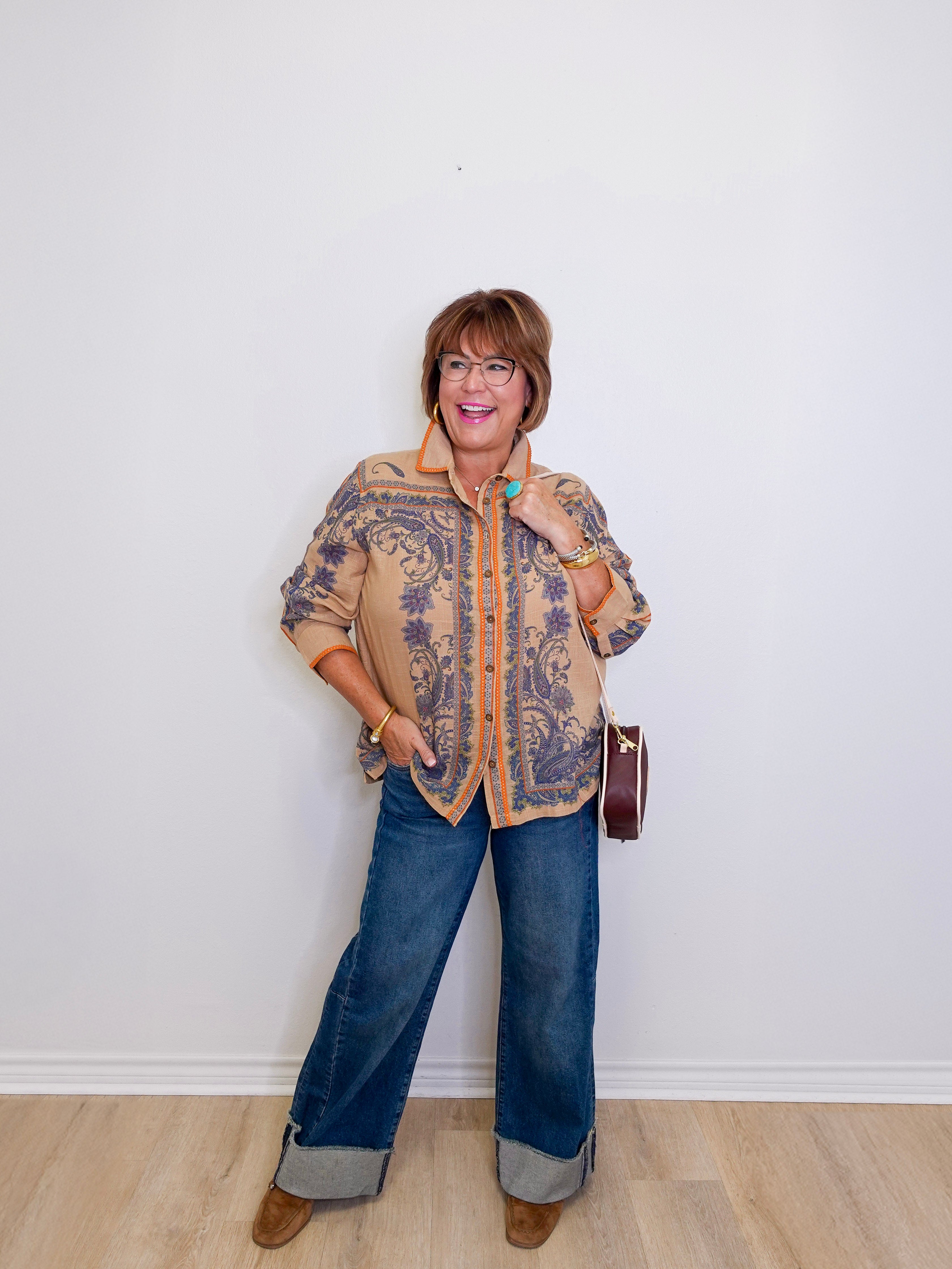 Woman wearing a patterned jacket and blue jeans against a white wall