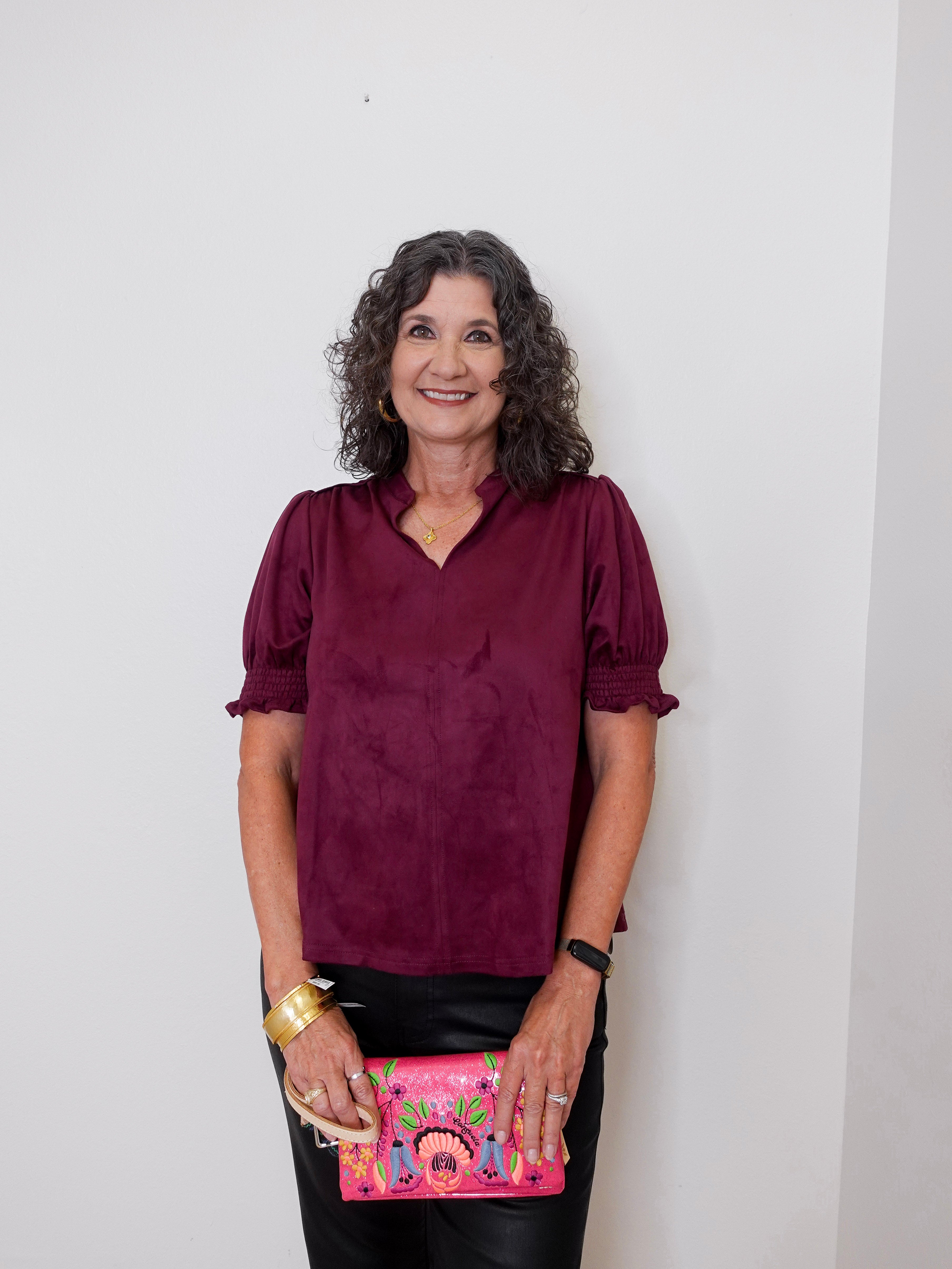 Woman wearing a burgundy blouse holding a colorful clutch against a plain background