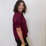 Woman wearing a burgundy blouse against a white wall