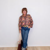 Person wearing a patterned shirt and jeans, standing against a white wall.